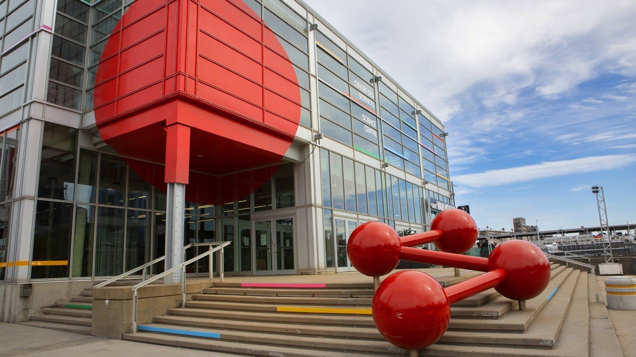 Modern building with red geometric elements and large molecule-like sculpture outside.