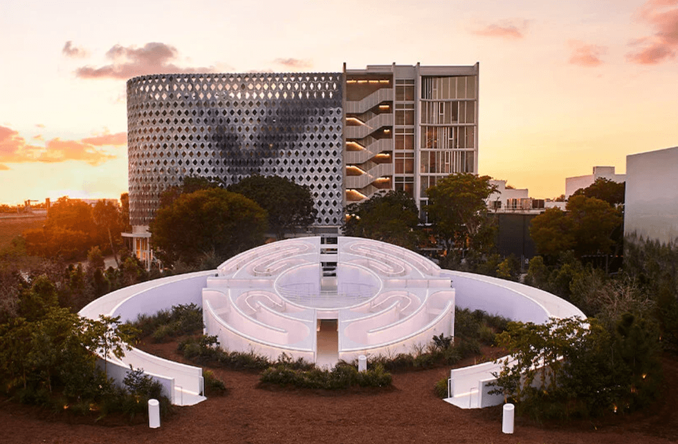 Modern buildings with a circular maze garden at sunset.