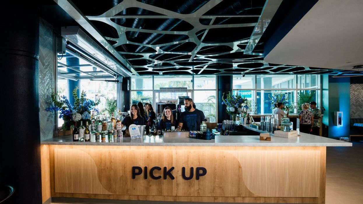 Modern cafe counter with "Pick Up" sign, staff behind, and bottles on display.