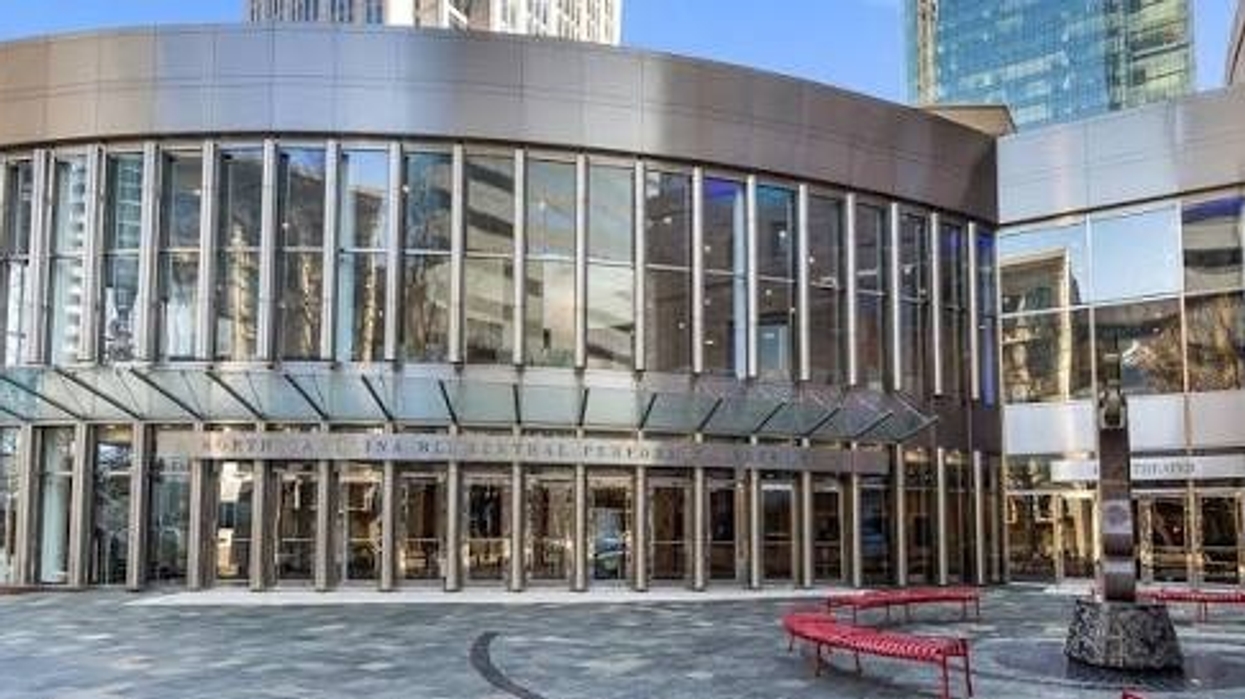 Modern circular glass building entrance with red benches and artwork on the right.