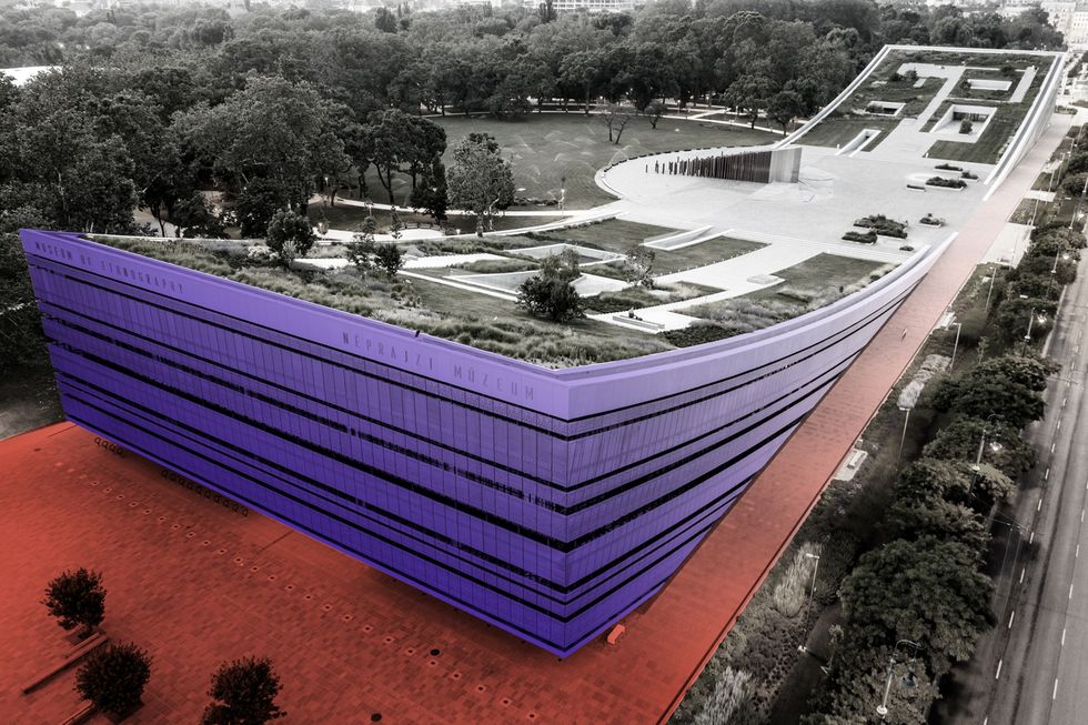 Modern curved building with green rooftop and park surroundings.