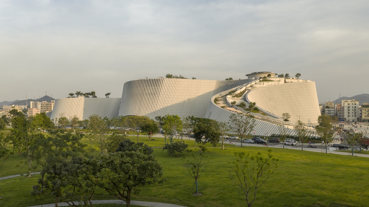 Modern curvilinear building, Shenzhen Natural History Museum, with a rooftop garden and surrounding greenery.