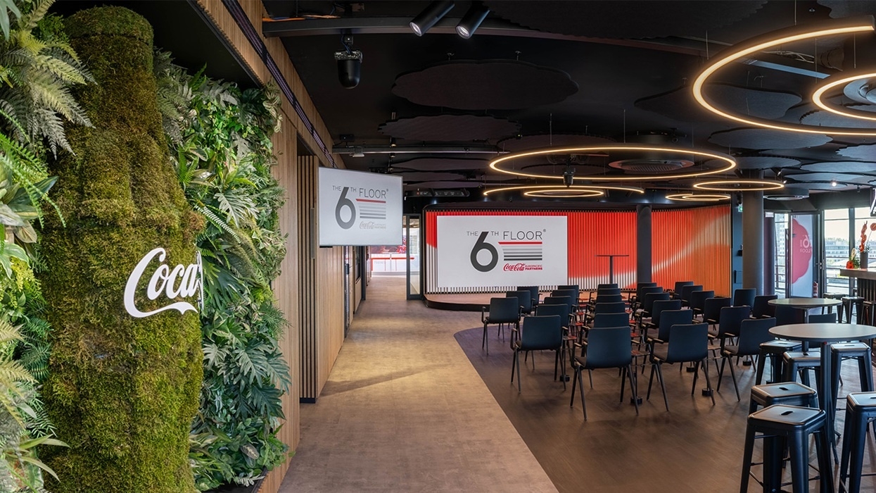 Modern customer experience centre from Coca-Cola, with greenery, circular lights, and rows of chairs facing a stage.
