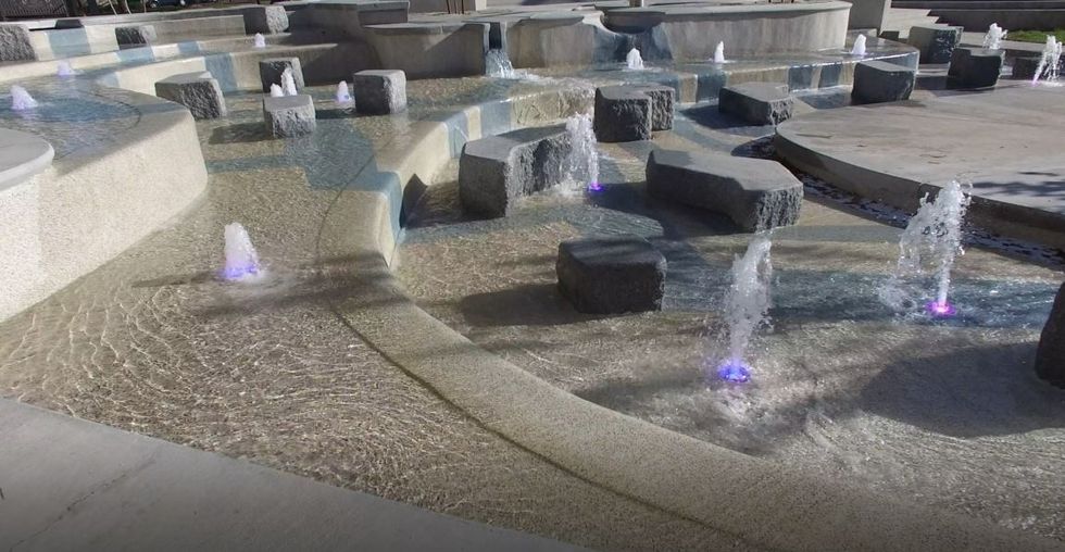 Modern fountain with geometric stone design and colorful illuminated water jets.