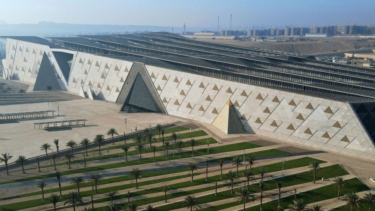 Modern, geometric building with triangular designs, surrounded by palm-lined paths and green areas.