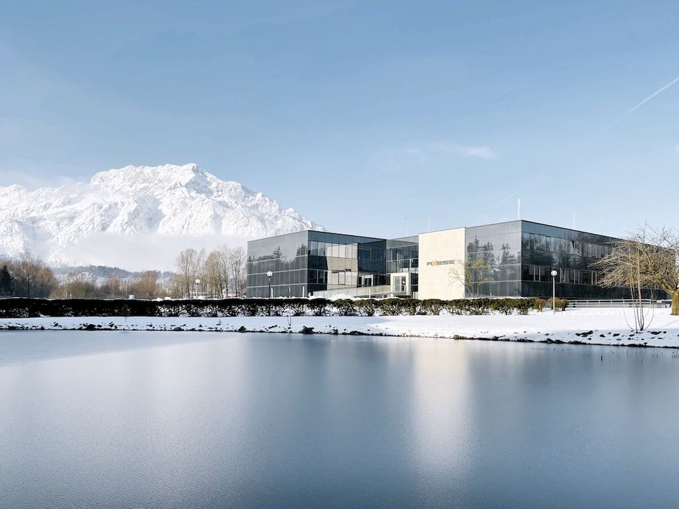 Modern glass building by a snowy lake with a mountain backdrop.