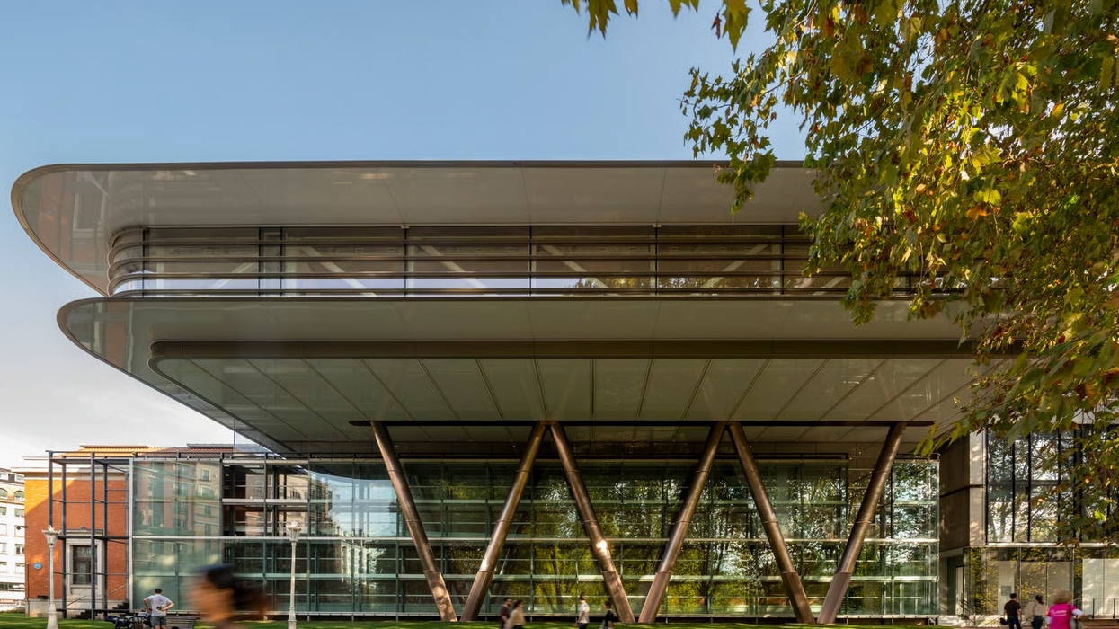 Modern glass building with overhanging floors and diagonal supports, surrounded by trees and people.