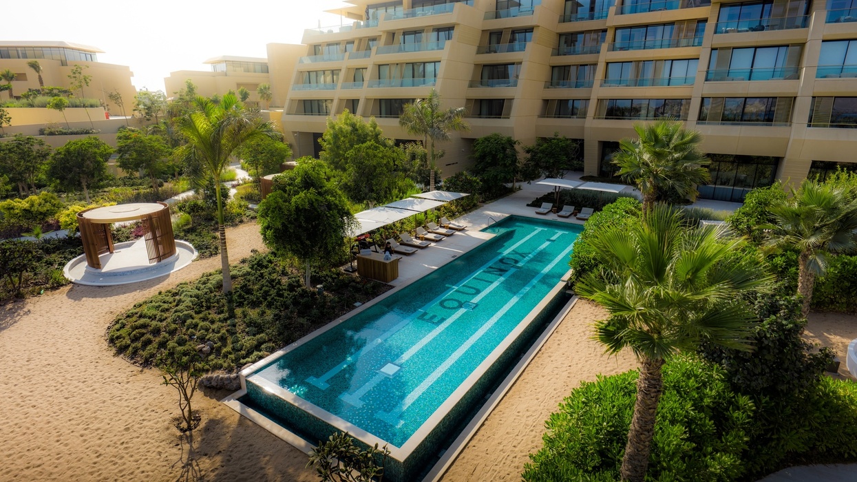 Modern hotel courtyard with a pool, lounge chairs, and lush greenery at Equinox Resort Amaala
