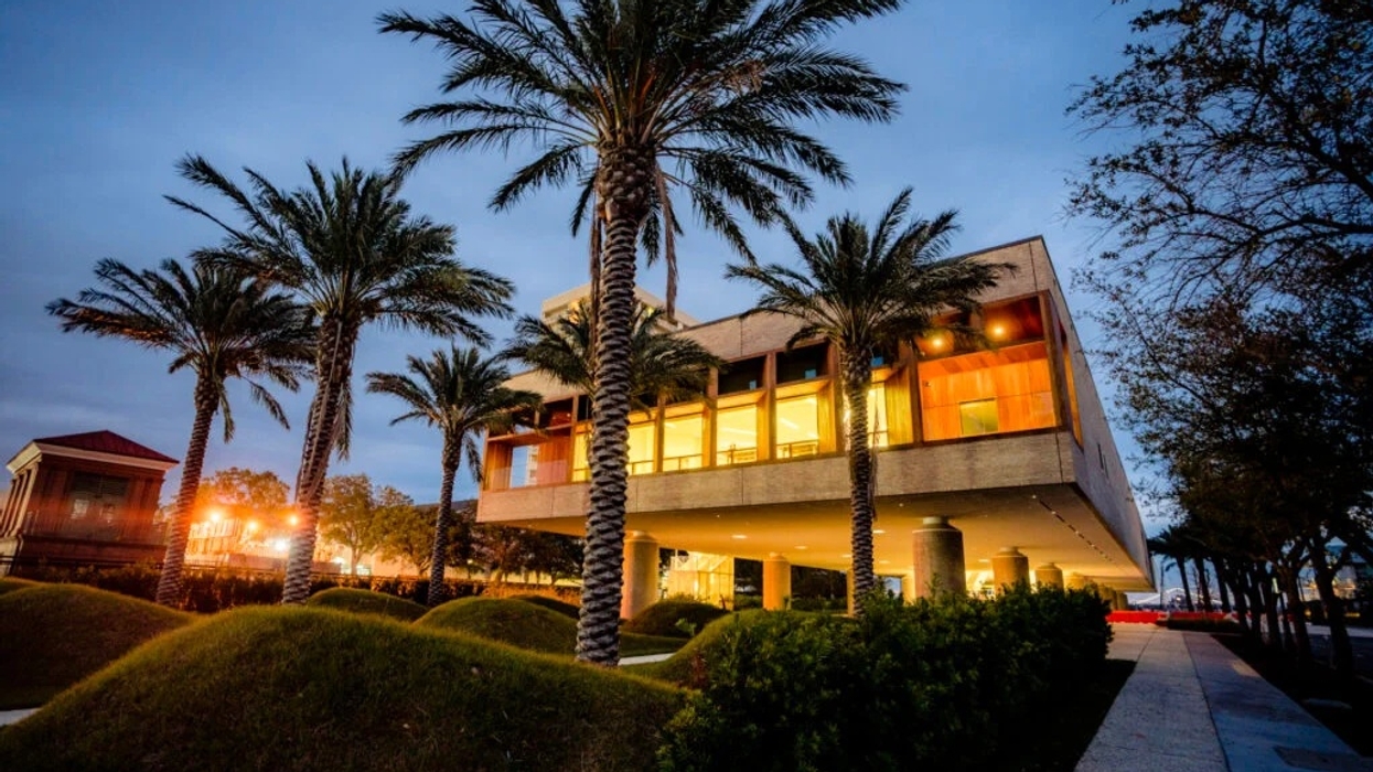 Modern, illuminated building called the International African American Museum surrounded by palm trees at dusk.