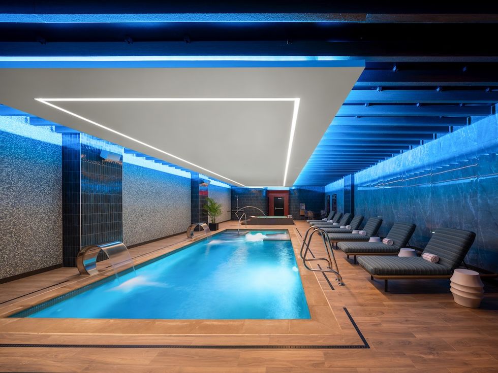 Modern indoor pool with loungers, blue lighting, and sleek design.