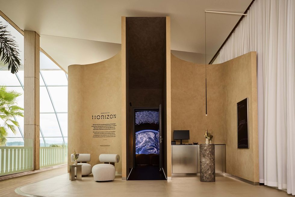 Modern interior with curved walls, seating, and digital display inside a bright, airy space.