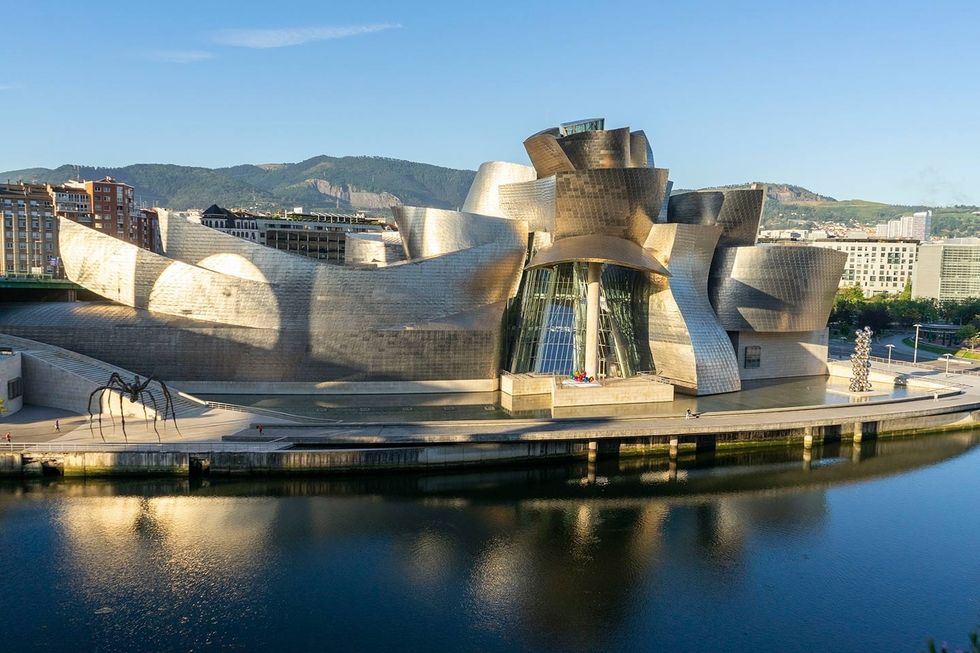 Modern metallic building called Guggenheim Bilbao by the water with mountain views and urban surroundings.