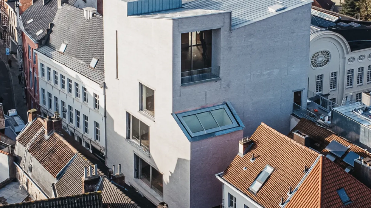 Modern multi-story building with large windows amidst traditional European rooftops.