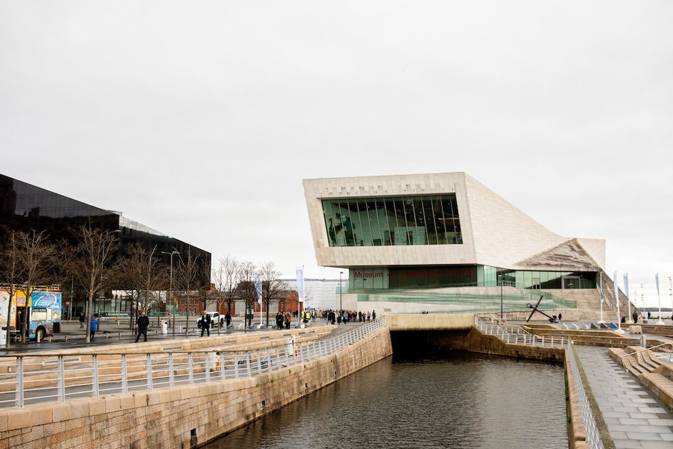 Modern museum building by a waterfront canal, with cloudy sky and pedestrians.