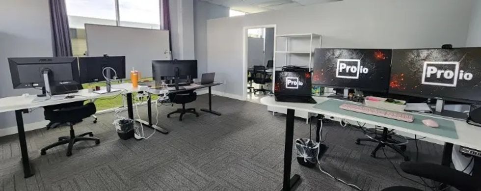 Modern office with desks, monitors, and computers, featuring "ProIO" on screens.