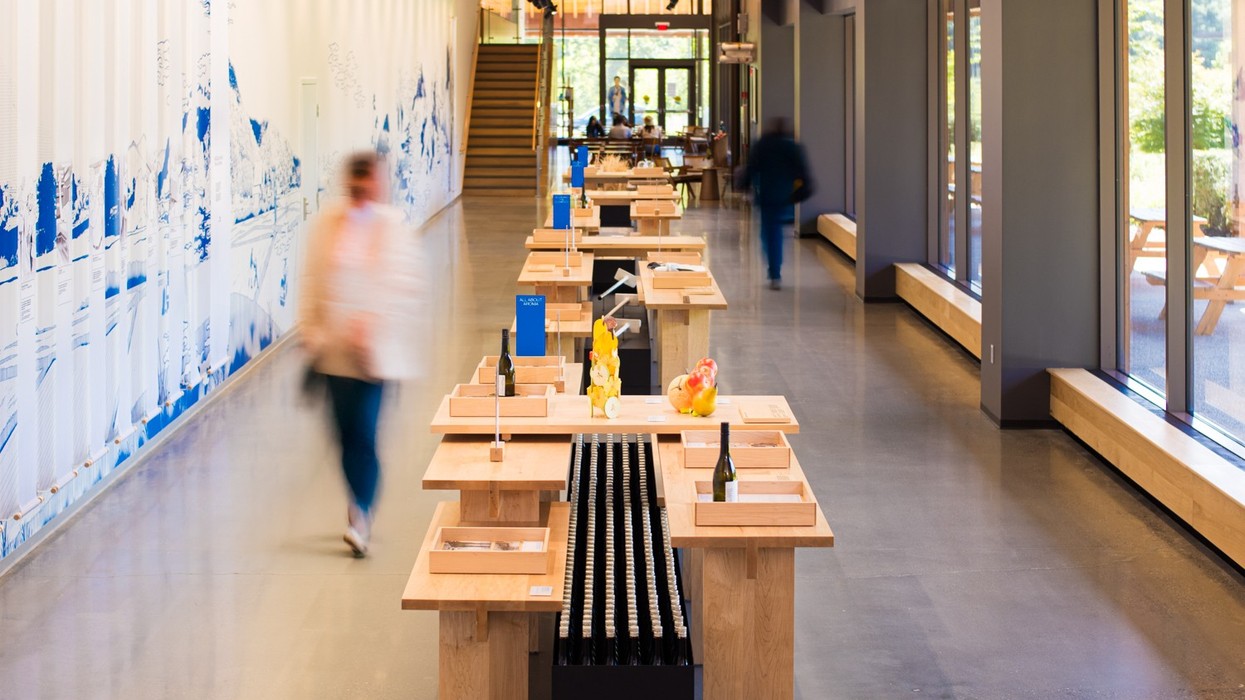 Modern open wine tasting room with wooden tables and blurred figures walking through.