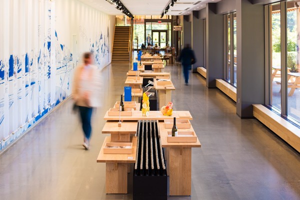 Modern open wine tasting room with wooden tables and blurred figures walking through.