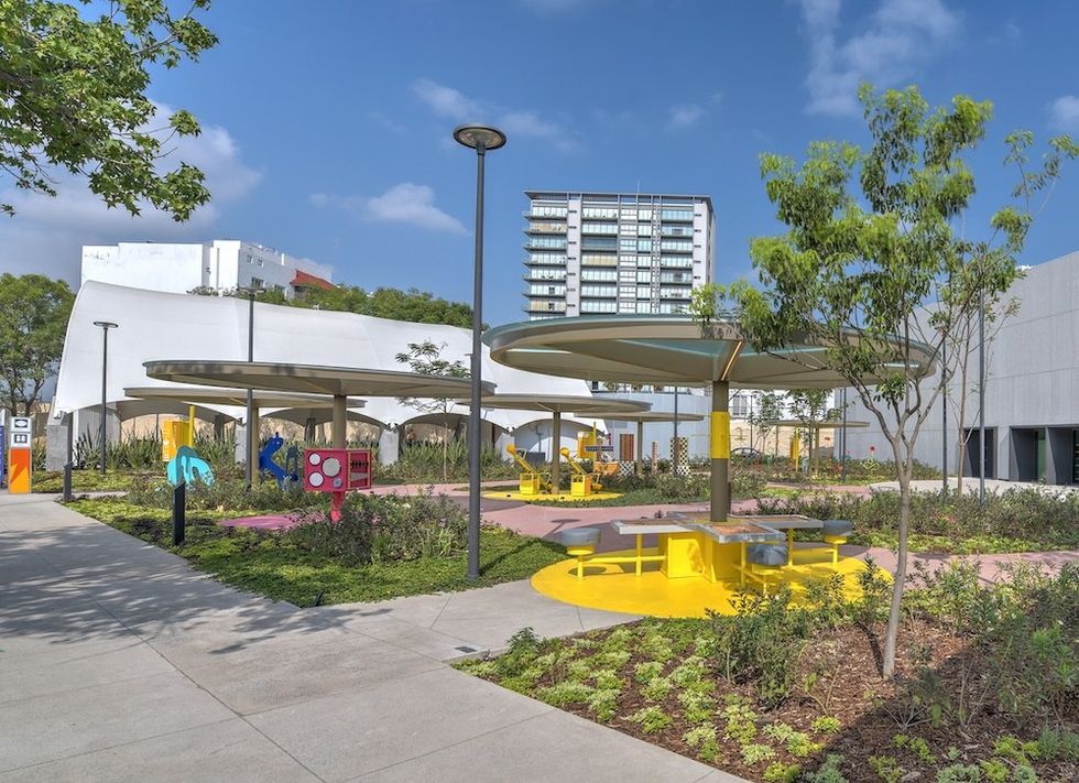 Modern playground with colorful structures and shaded benches, surrounded by greenery.