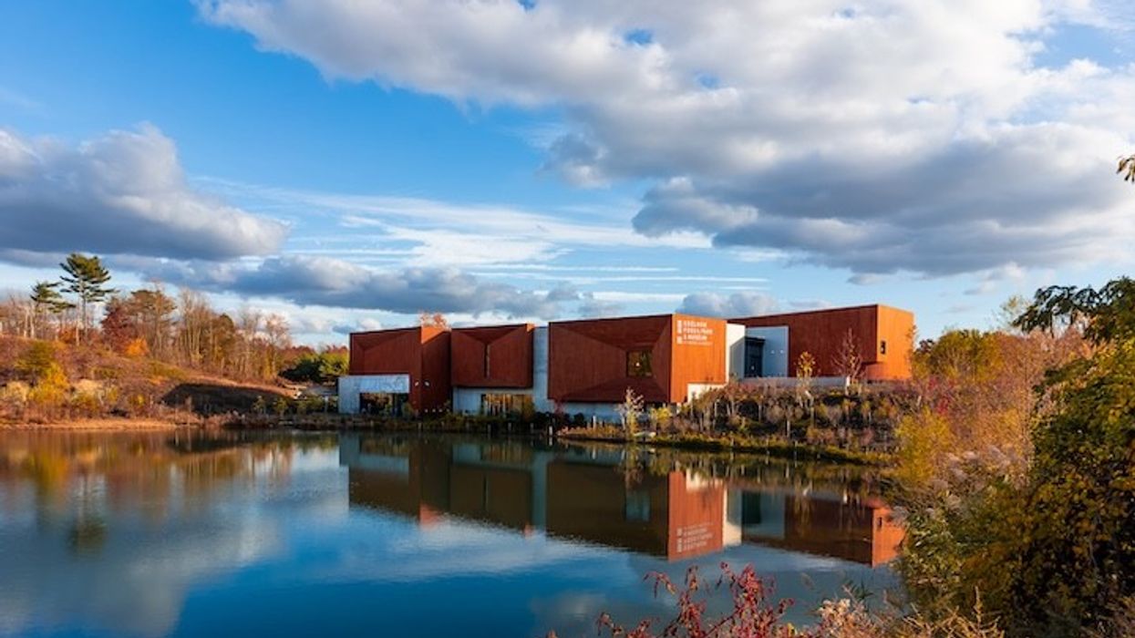Modern red building reflected in a serene lake under a partly cloudy sky.