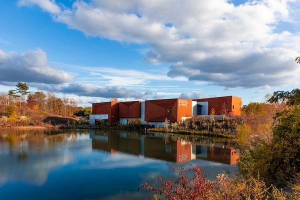Modern red building reflected in a serene lake under a partly cloudy sky.