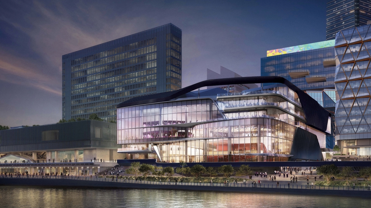 Modern riverside building called the WestK Performing Arts Centre with glass facade, surrounded by city skyscrapers at dusk.