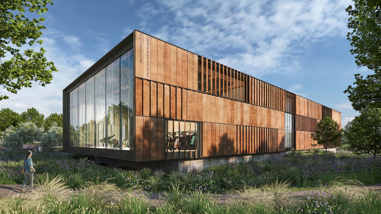 Modern, rust-colored building called the Bruce Springsteen Center for American Music with large windows, surrounded by greenery and under a blue sky.