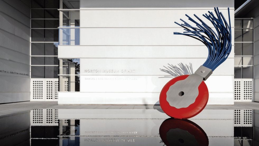 Modern sculpture resembling a blue whisk on a red base, outside Norton Museum of Art.