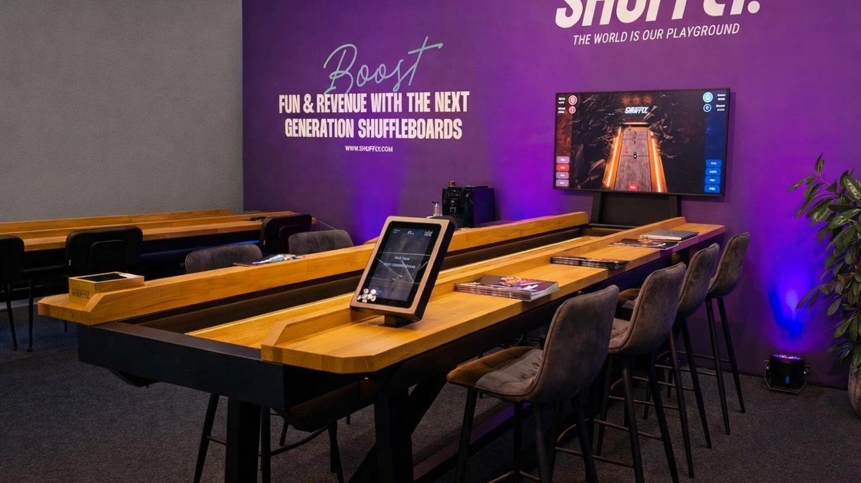 Modern shuffleboard setup with digital screen and tablet in a stylish room with purple accents.