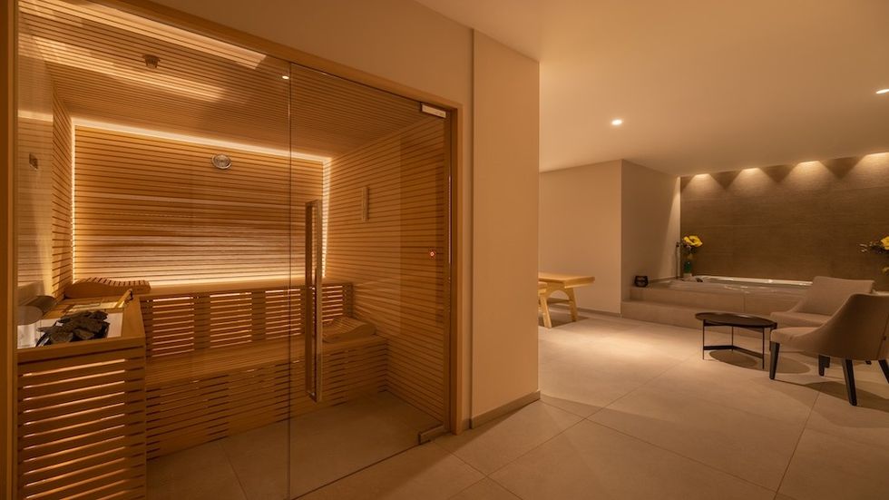 Modern spa room with a wooden sauna and a hot tub area, softly lit and inviting.