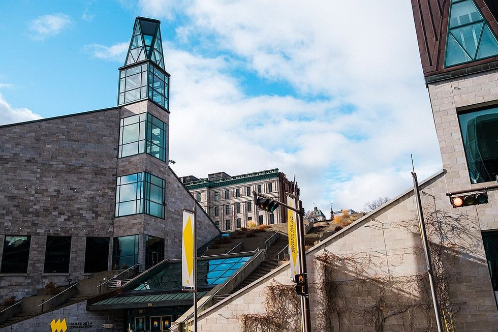 Modern stone building with glass tower against a bright cloudy sky.