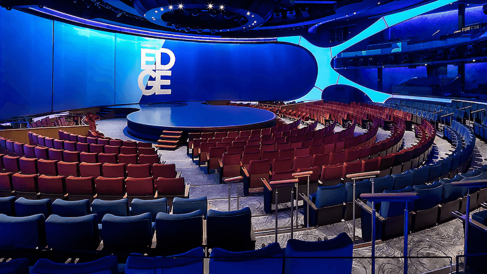 Modern theater with circular stage, tiered seating, and blue ambient lighting.