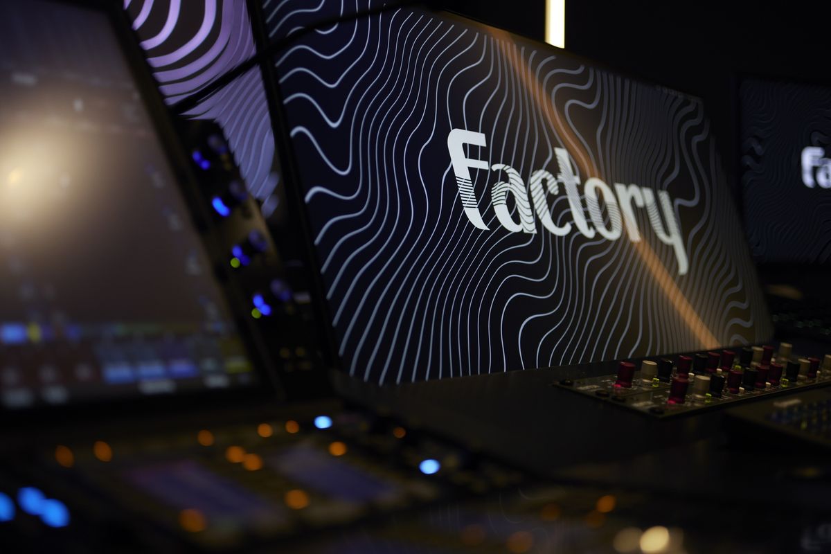 Monitors with "Factory" text and wavy lines in a dark, high-tech studio.