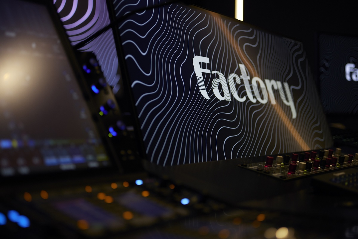 Monitors with "Factory" text and wavy lines in a dark, high-tech studio.