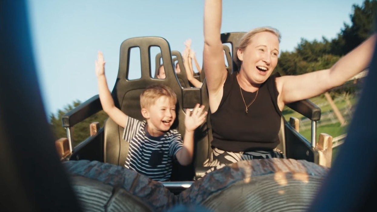 Mother and child joyfully riding a roller coaster with arms raised.