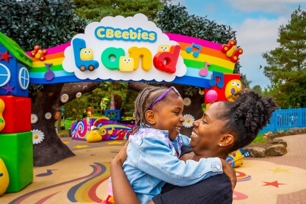 Mother and daughter smile at CBeebies Land entrance, colorful and cheerful setting.