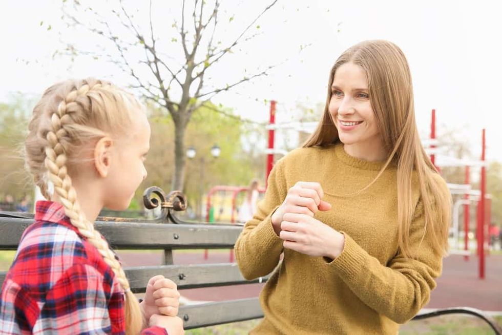 mother and daughter using sign language on a park bench
