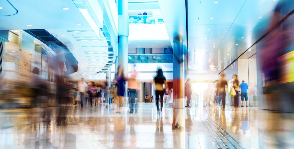 Motion-blurred shoppers walk through a bright, modern mall atrium.