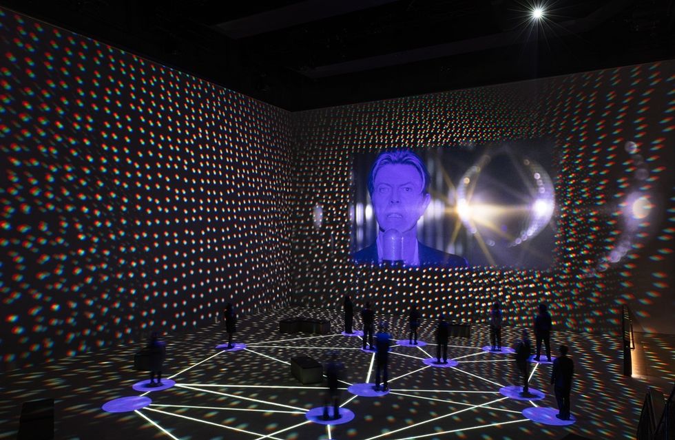 Multicolored light patterns and a projected face in a dark room with figures on light circles.