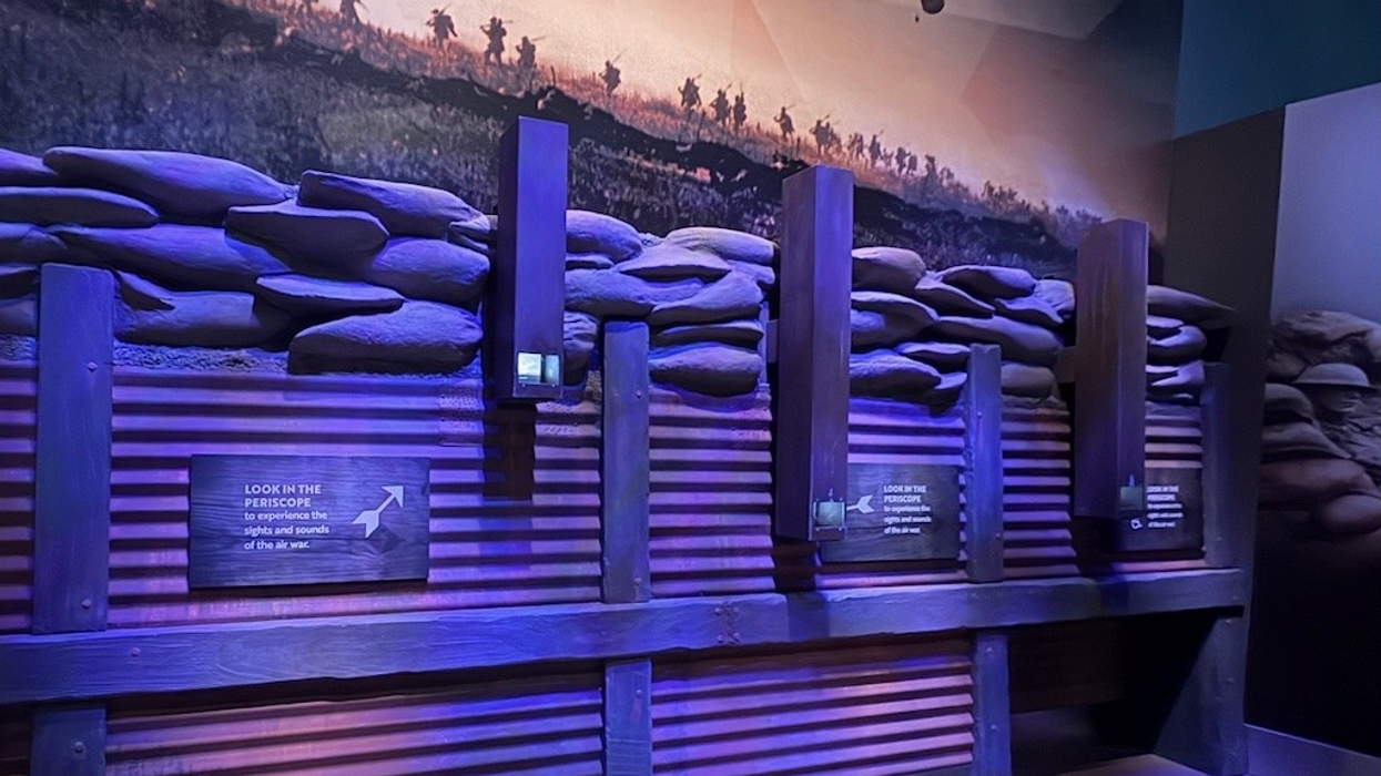 Museum exhibit of a WWI trench with sandbags and mural of soldiers in battle.