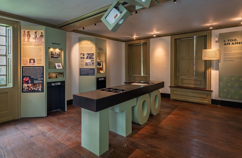 Museum exhibit room with informational displays and a central table marked "I TOO" at the Edward W. Kane & Martha J. Wallace Center for Black History.