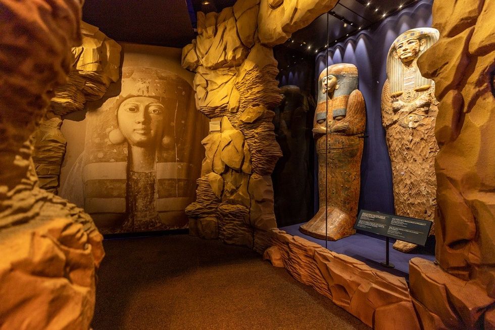 Museum exhibit with ancient Egyptian sarcophagi and a large pharaoh mural.