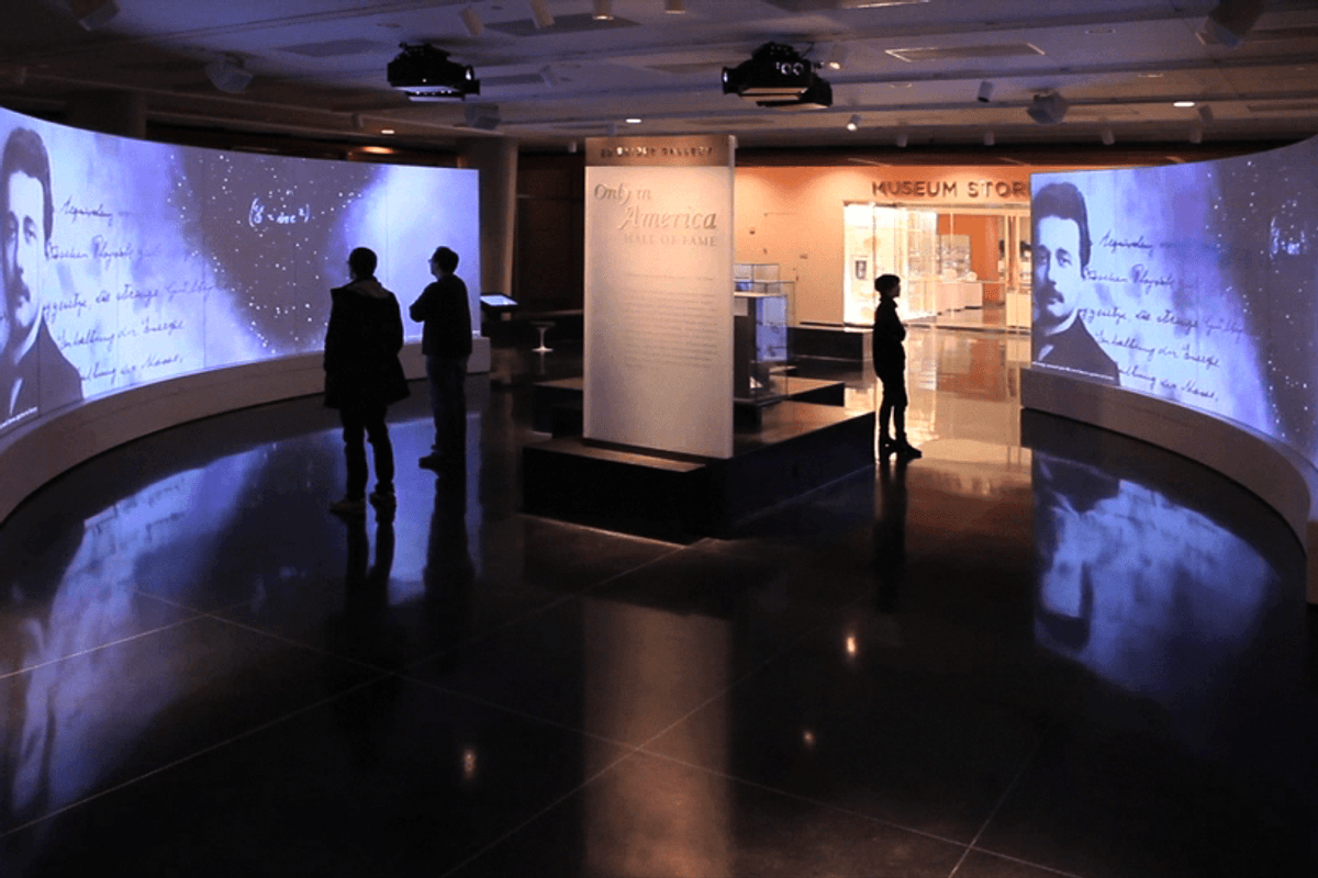 Museum exhibit with curved screens displaying historical portraits and text.