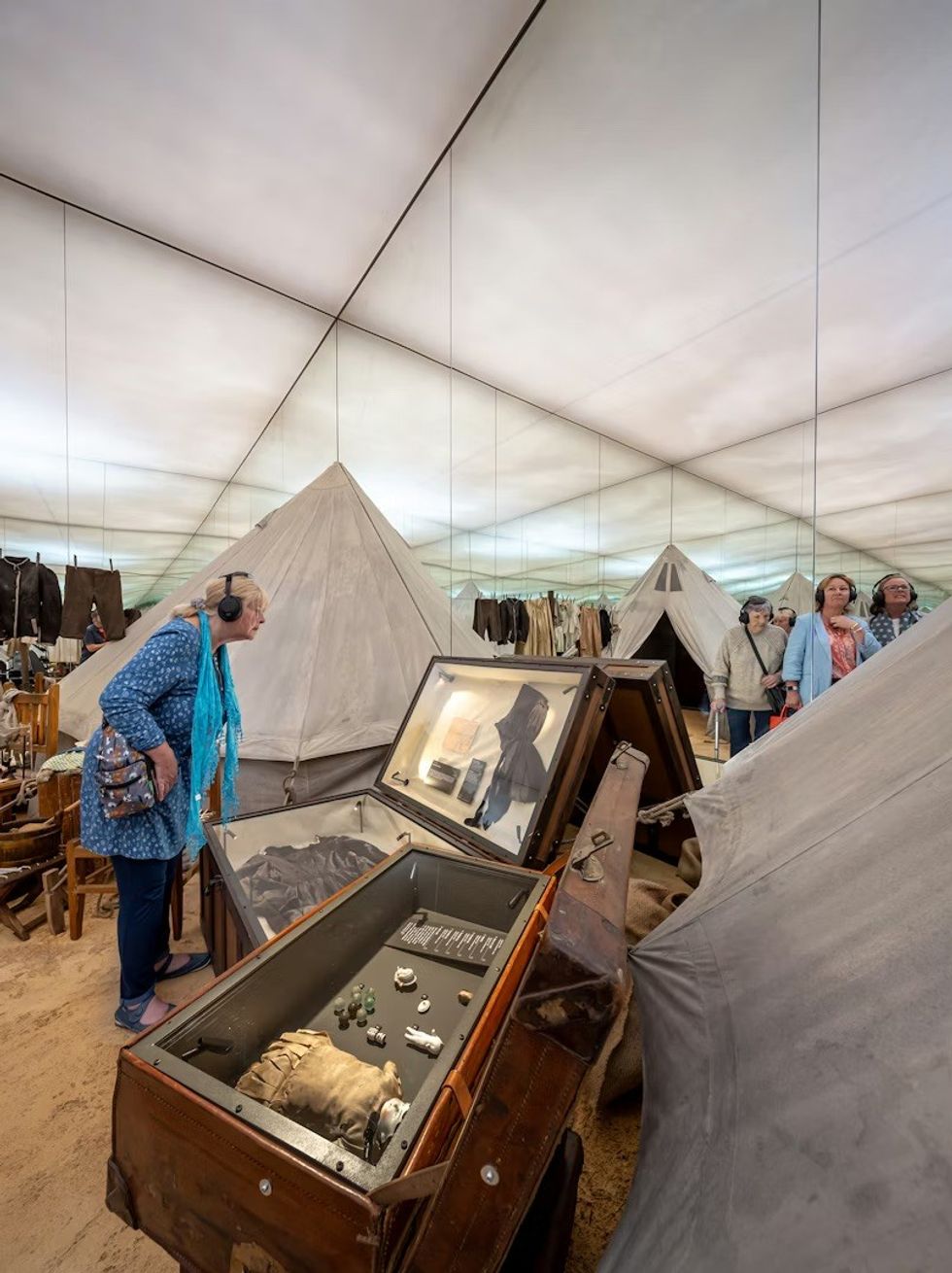 Museum exhibit with tents, artifacts in cases, and visitors wearing headphones. The War Rooms at The Story of Emily