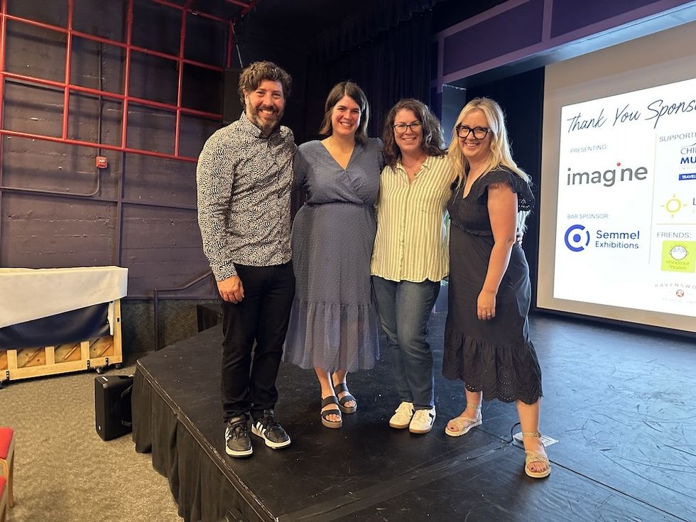 Museum EXP team smiling on stage with a sponsor board in the background.