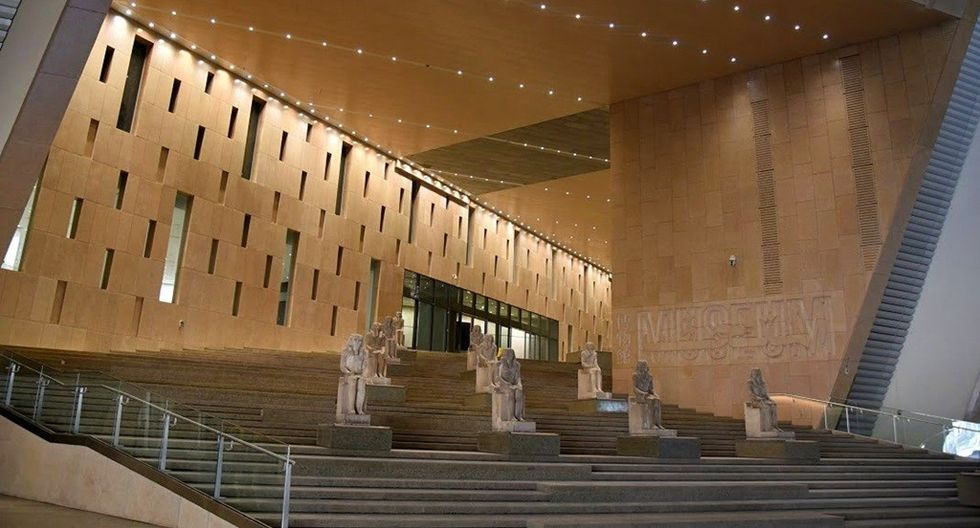 Museum interior with statues on wide, modern stairs and illuminated walls.