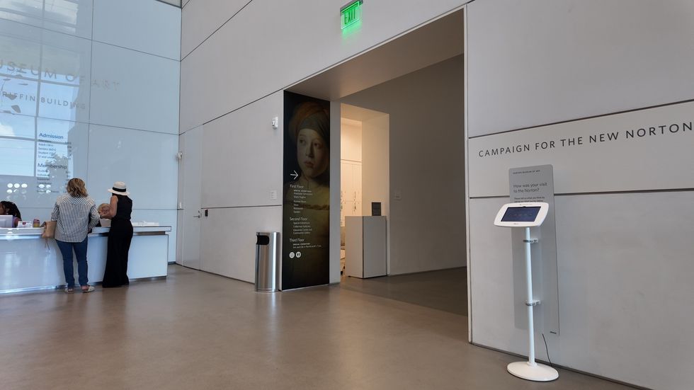 Museum lobby with visitors, information desk, and exhibit entrance.