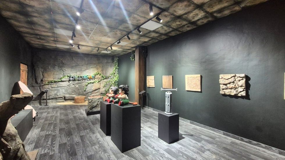Museum room with sculptures on pedestals, wall art, and rustic stone wall design.