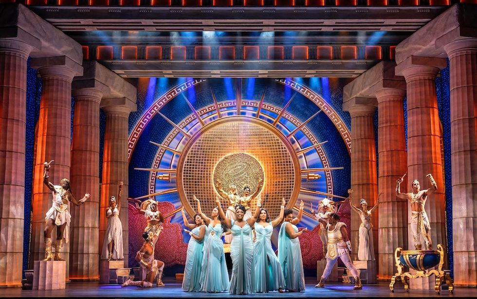 Musical stage with performers in blue dresses, surrounded by Greek-style columns and statues.