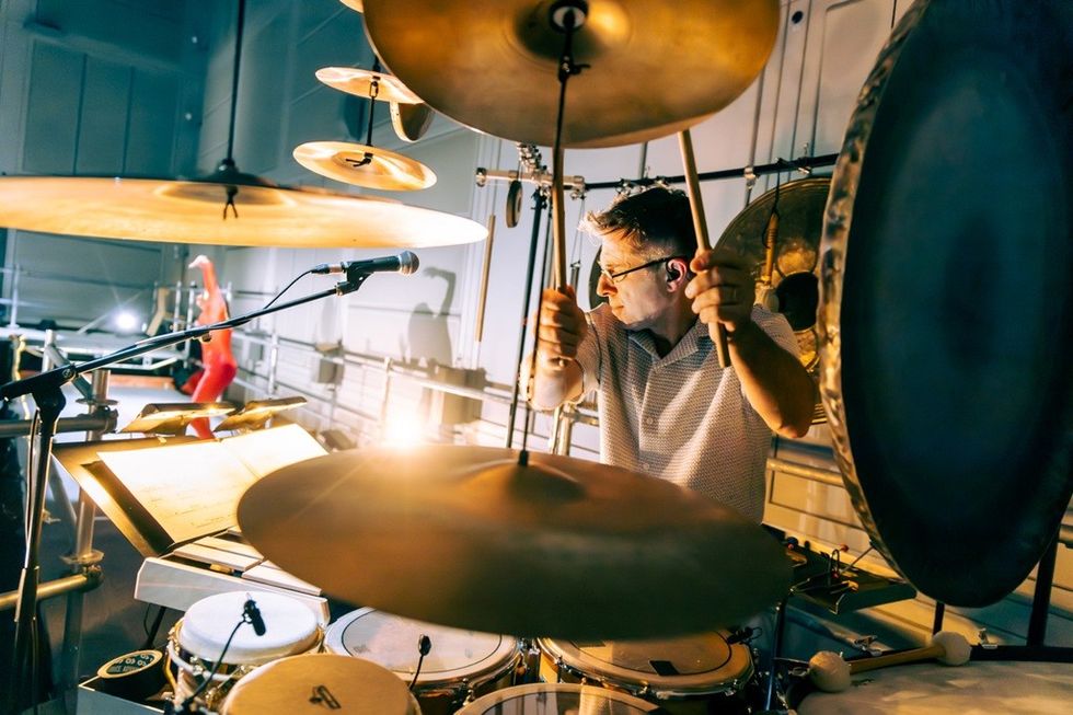 Musician playing drums and cymbals passionately, with stage lights and microphone.
