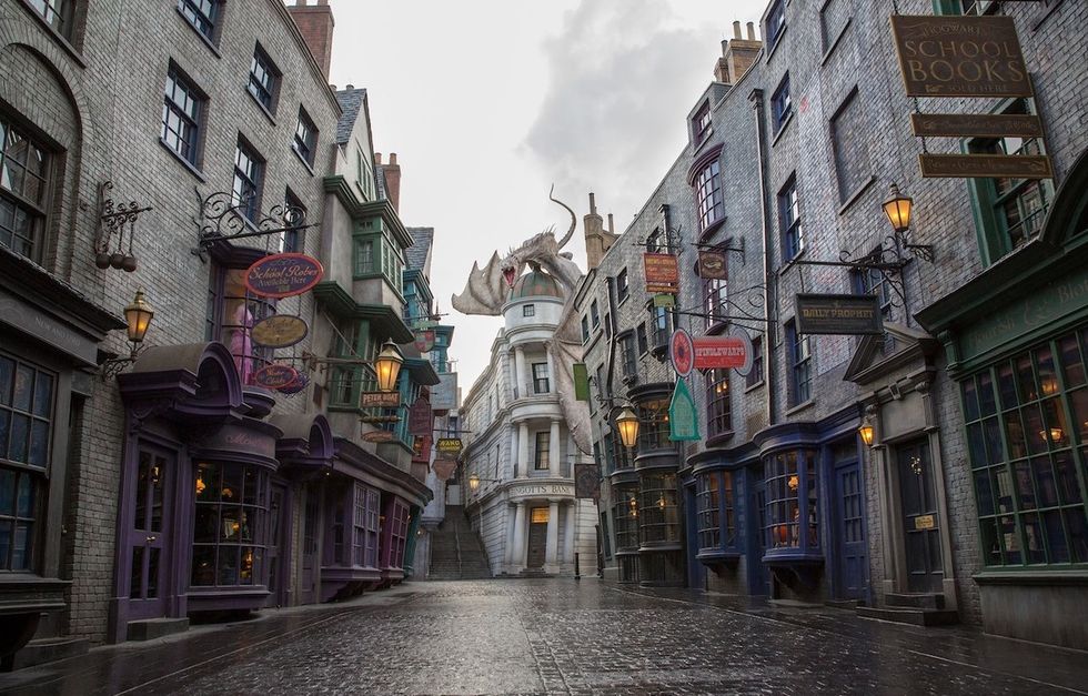 Narrow cobblestone street with a dragon atop a white building, surrounded by shops.